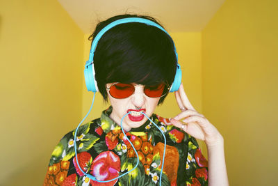 Young woman wearing blue headphones standing against yellow wall