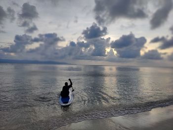 Rear view of man standing at beach against sky during sunset