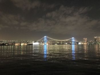 Illuminated bridge over river against sky in city at night