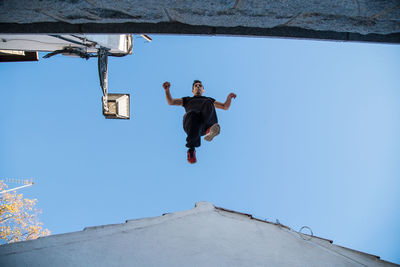 Low angle view of man jumping on rooftop