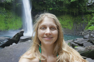 Portrait of smiling young woman against waterfall