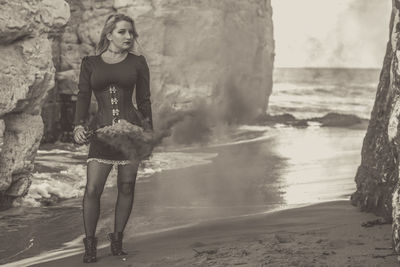 Portrait of young woman with distress flare standing by rock formations at beach