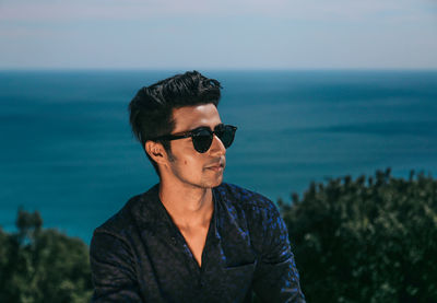 Young man wearing sunglasses looking at sea against sky