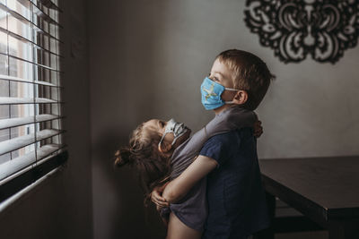 Lifestyle portrait of young siblings with masks on hugging at home negative space