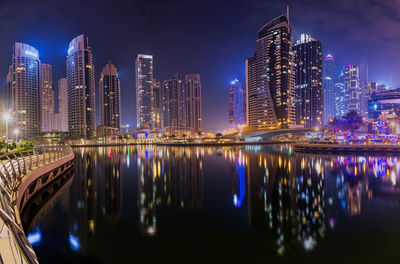 Illuminated buildings by river against sky in city at night