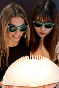 Multi-ethnic female couple of girlfriends are looking at a magical bright book indoors