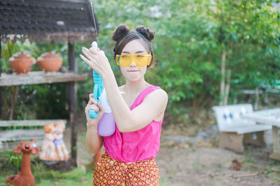 Portrait of young woman holding squirt gun while standing in yard