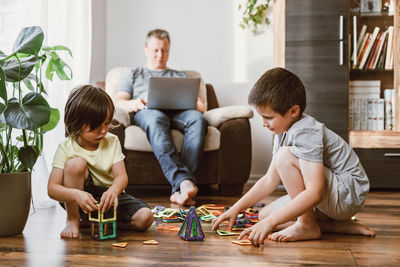 Remote work at home. children play with toys, and a young businessman, dad works at a laptop 