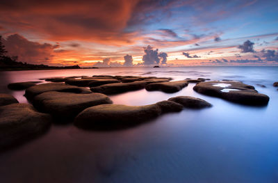 Rocks at sea against sky during sunset