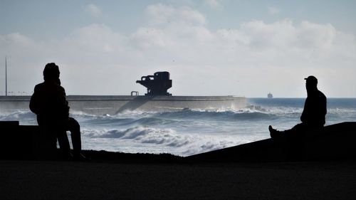 Silhouette of seaport crane at beach against sky