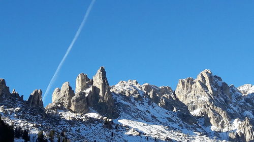 Low angle view of snowcapped mountains against clear blue sky