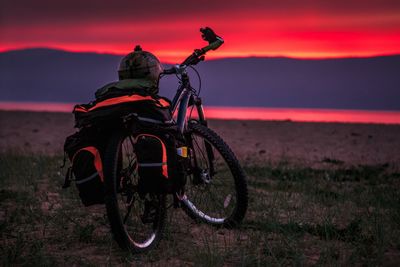 Bicycle parked on land against sky during sunset