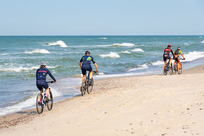 Men riding bicycle on beach against sky