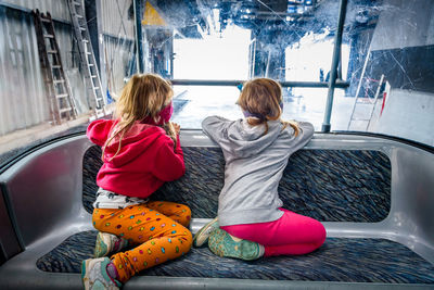 Rear view of girls looking through window while sitting on vehicle seat