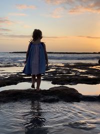 Rear view of a girl standing on beach during sunset