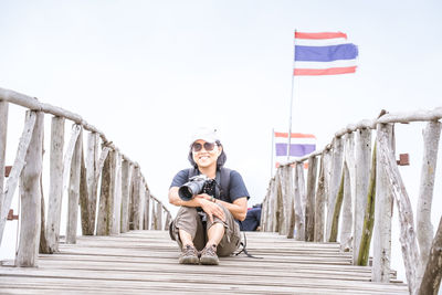 Portrait of smiling young man sitting on staircase against sky