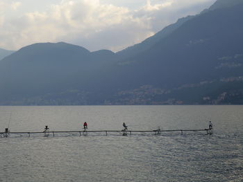 People sitting on jetty for fishing against cloudy sky