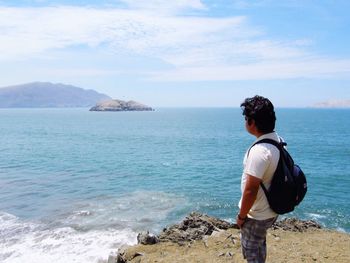 Side view of man with backpack standing on cliff against sky