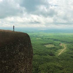 Mid distance view of man standing on cliff against cloudy sky