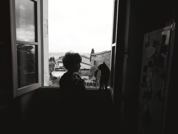 Rear view of kid and cat playing togheter near window