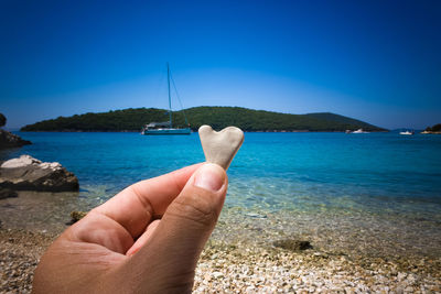 Cropped hand of person holding heart shape pebble at beach