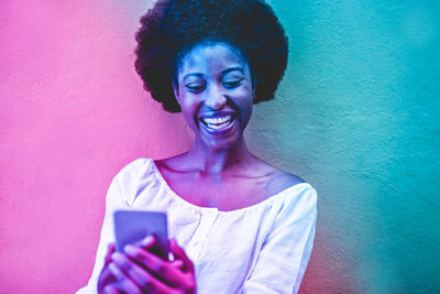 Cheerful young woman using mobile phone against wall
