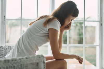 Woman looking away while sitting on window at home