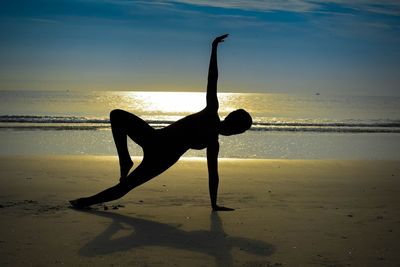 Silhouette woman on beach against sky during sunrise.