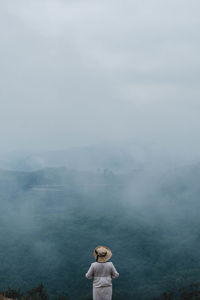 Rear view of woman standing on rock against sky