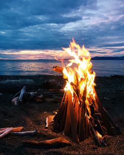 Bonfire by sea against cloudy sky at dusk