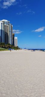 Scenic view of beach by buildings against blue sky