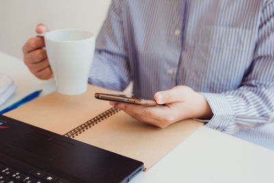 Midsection of man holding coffee cup on table