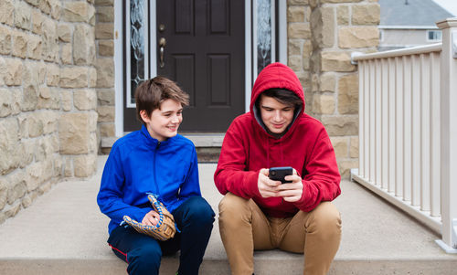 Two teenage boys sitting and talking on the front steps of a house.