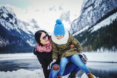 Smiling mother with daughter on snow during winter