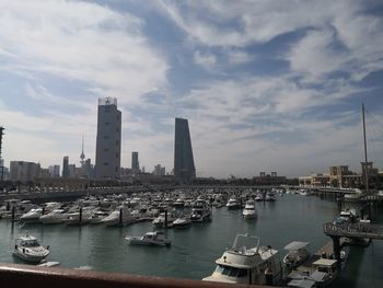 Boats moored in harbor by buildings against sky