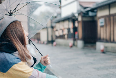 Midsection of woman holding umbrella on street in city