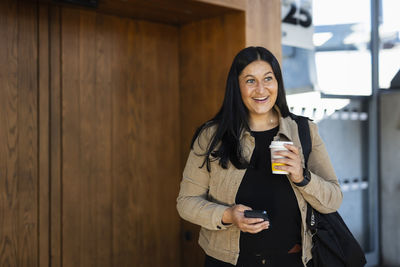 Smiling woman at train station holding disposable cup