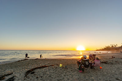 People on beach against clear sky during sunset