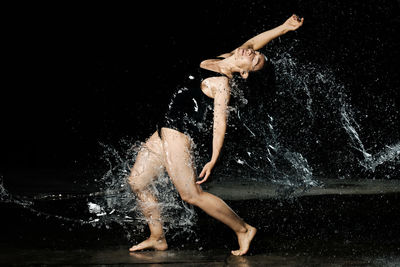 Side view of woman splashing water against black background