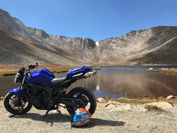 Bicycle by lake against mountain range against clear blue sky