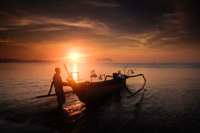 Silhouette fisherman with boat in sea against sky during sunset