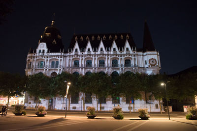 Illuminated building by street against sky at night