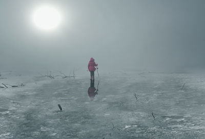 Rear view of woman standing on frozen lake against clear sky