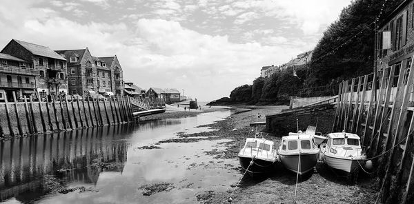 Boats moored on river by buildings against sky