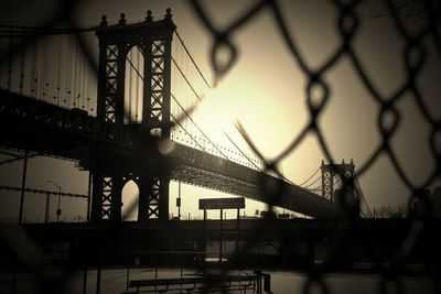 Manhattan bridge over east river against sky seen from chainlink fence