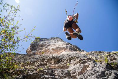 Low angle view of man rock climbing against sky