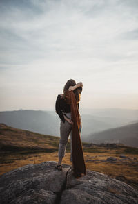 Man posing on rock looking at mountain against sky