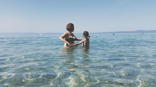 Mother with son standing at sea against clear sky during sunny day