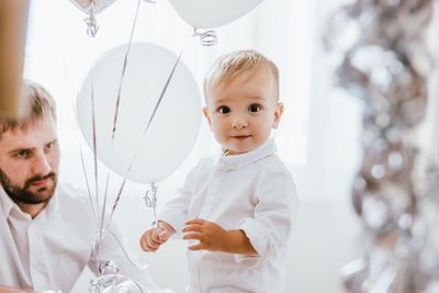 Portrait of baby boy holding balloons with father at home