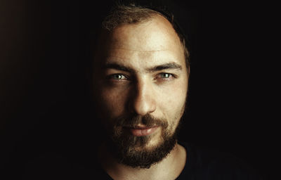 Close-up portrait of bearded young man against black background